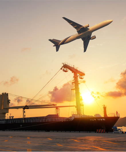 Airplane flying above a cargo ship at sunset